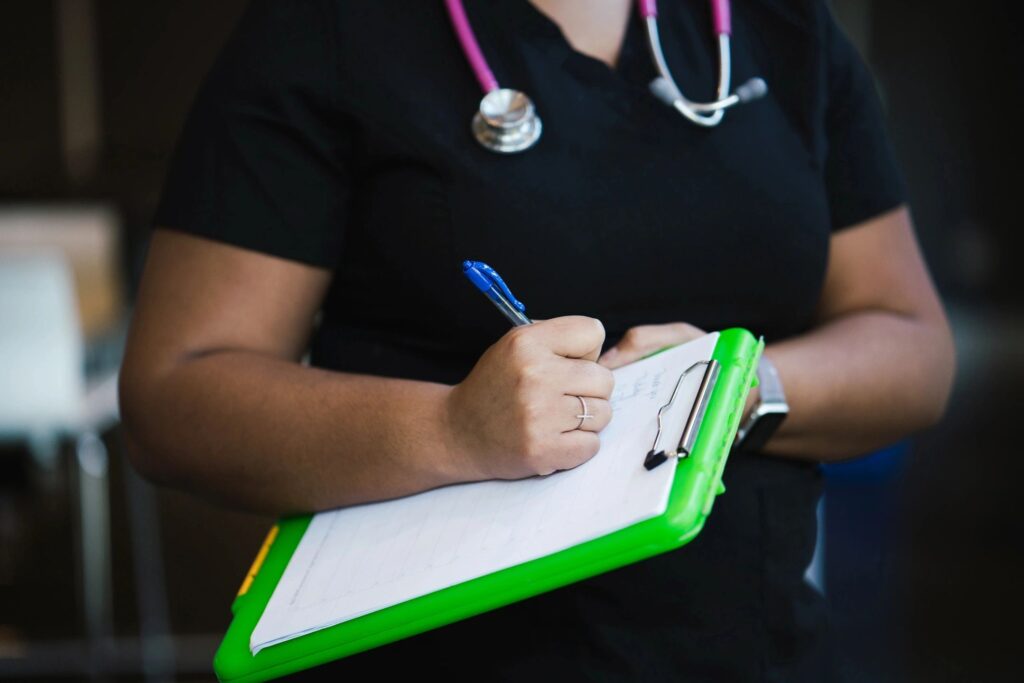 Nurse writing on a clipboard with a pen.